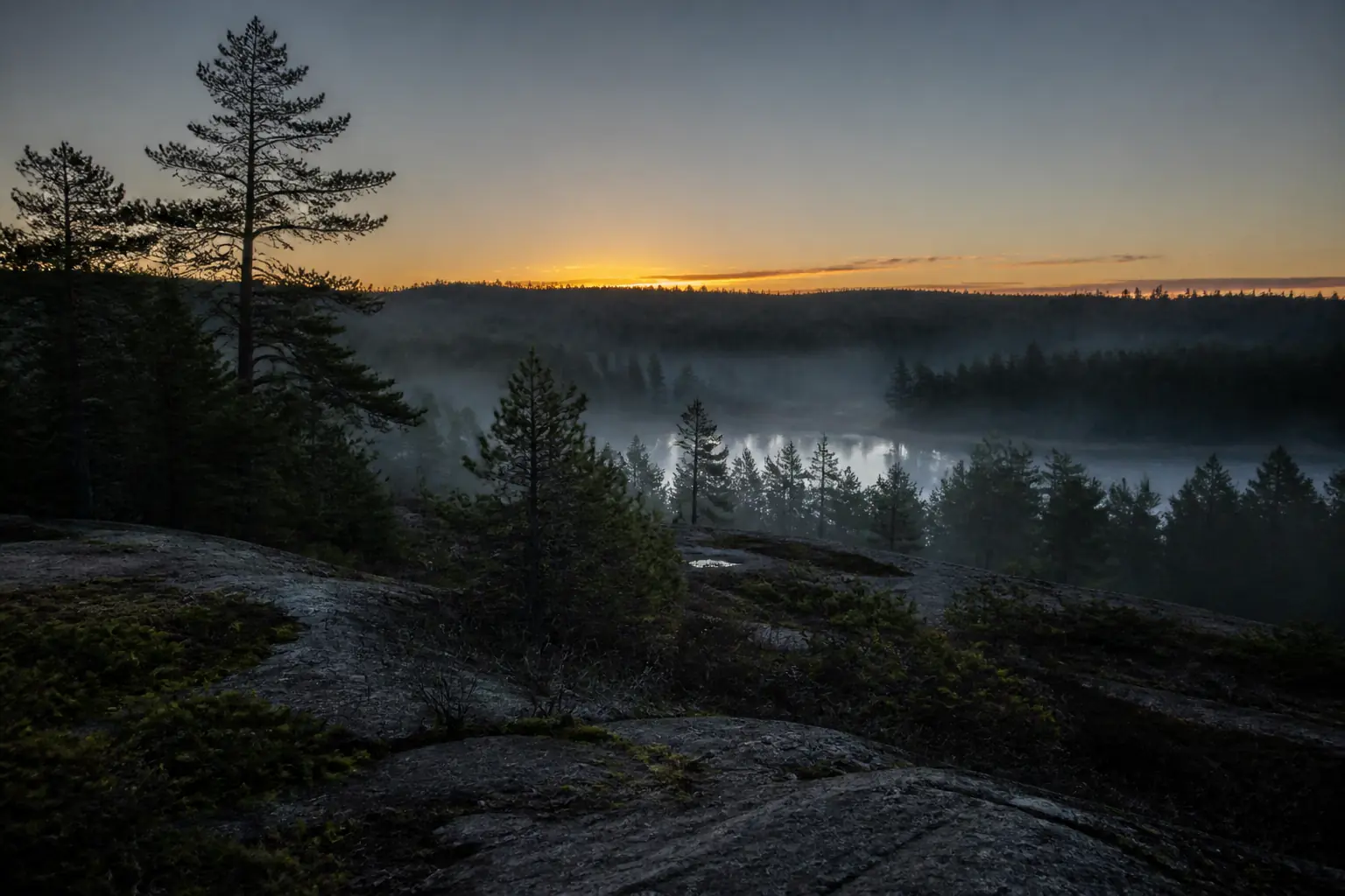 The sun just touching the far horizon over a misted pine valley
